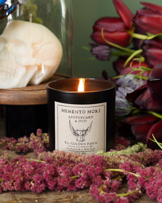 Candle with skull decoration surrounded by flowers on a wooden surface