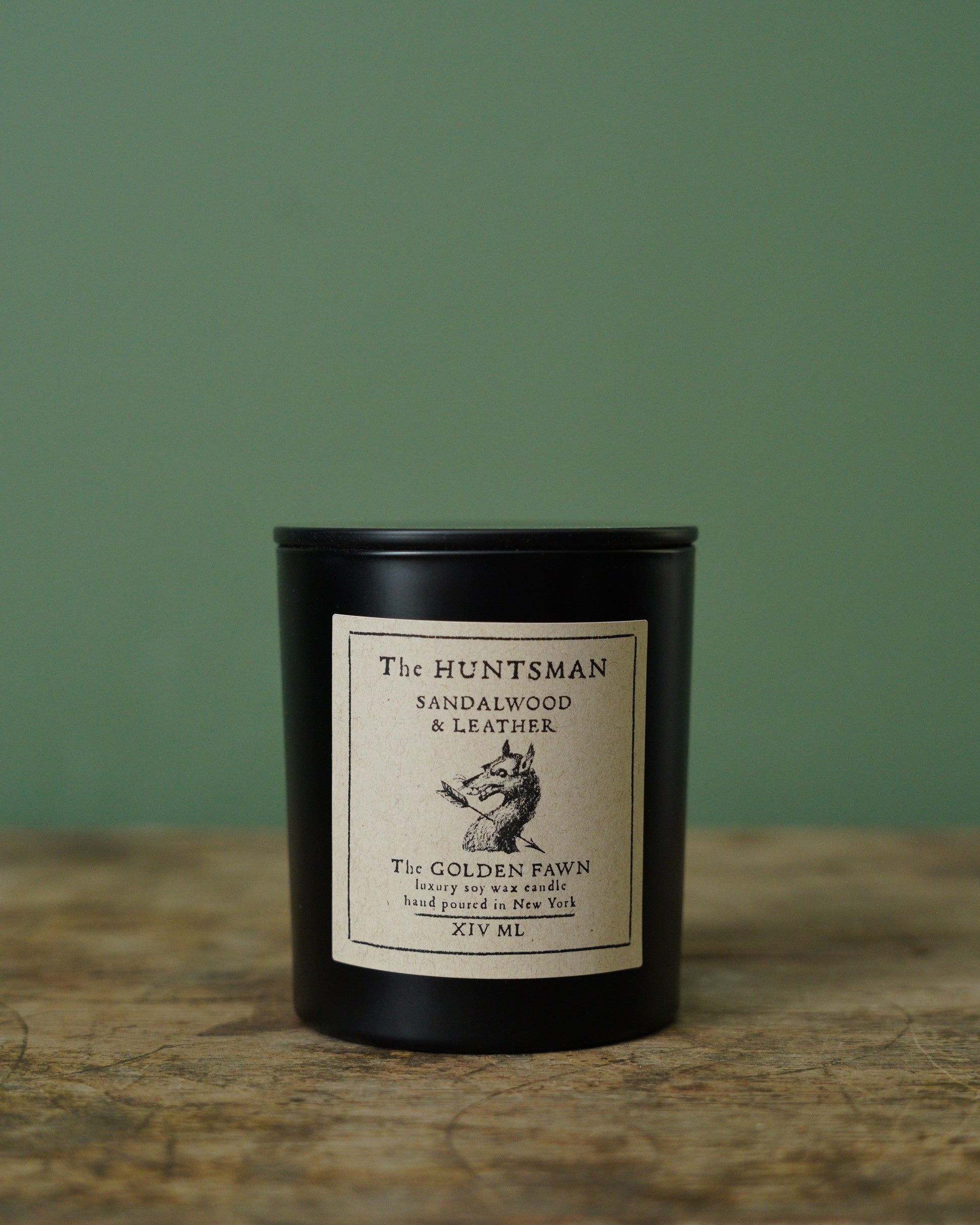 Black candle with a label on a wooden surface and green background