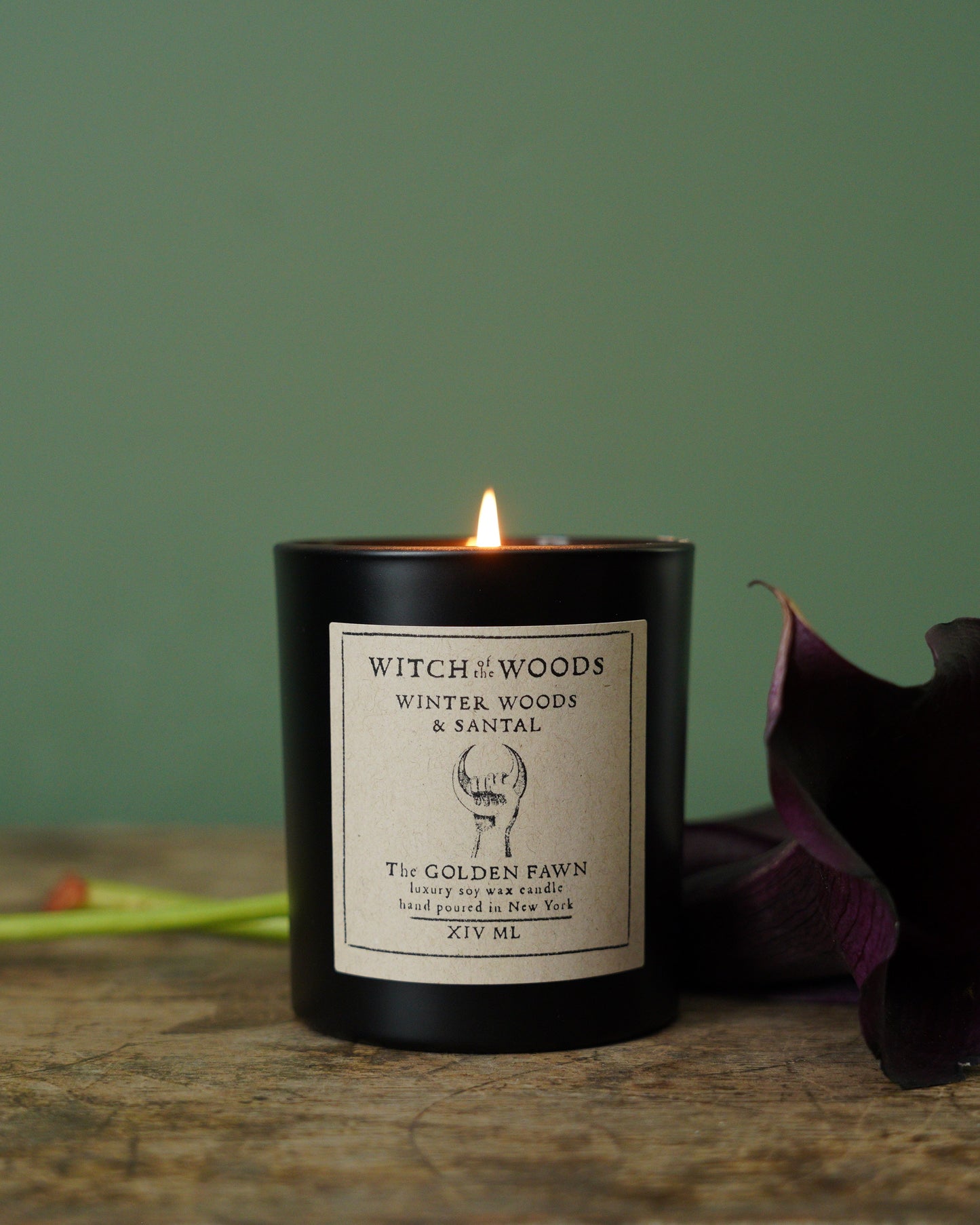 Candle with a label on a wooden surface against a green background