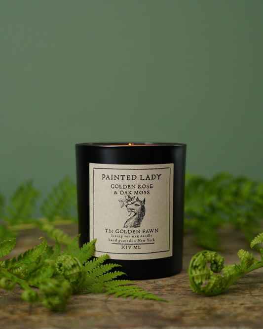 Candle with a label on a wooden surface with green foliage